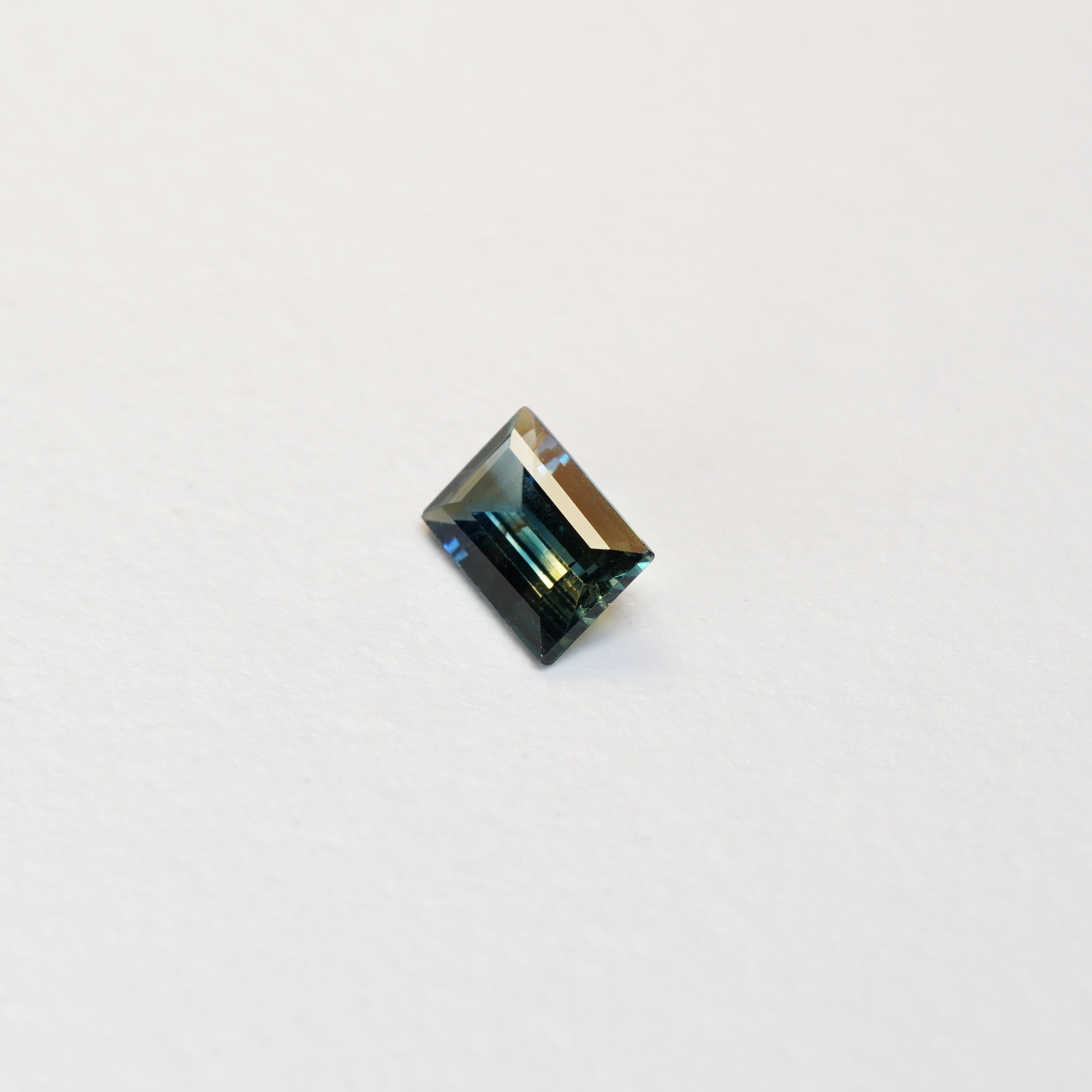1.1 carat baguette parti teal sapphire with mixed green and blue color.