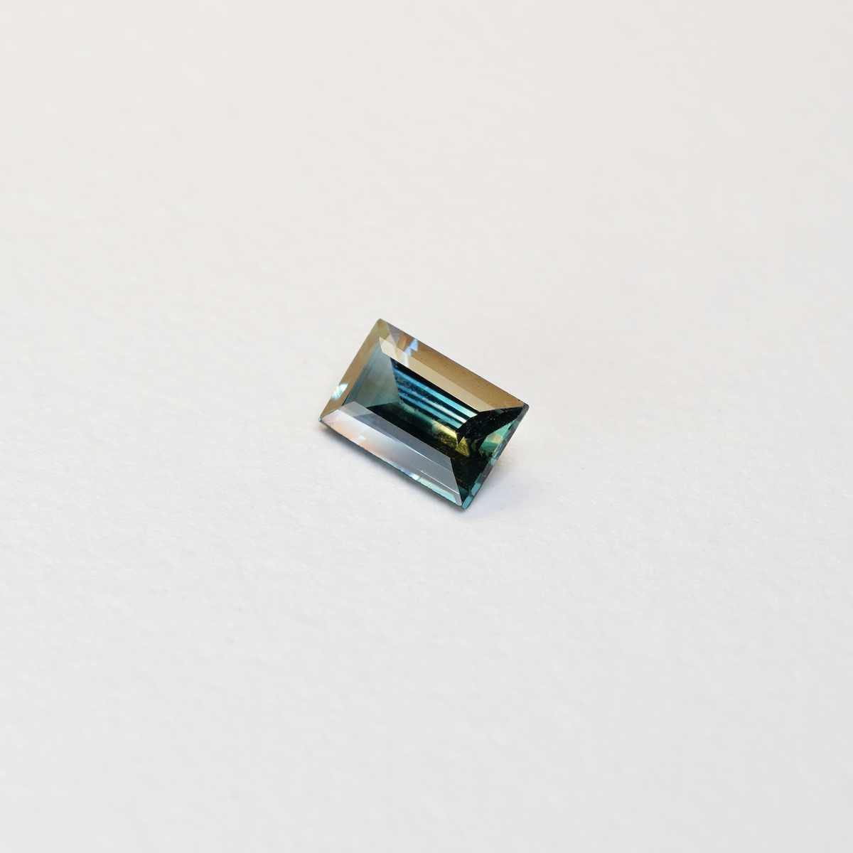 1.1 carat baguette parti teal sapphire with mixed green and blue color.