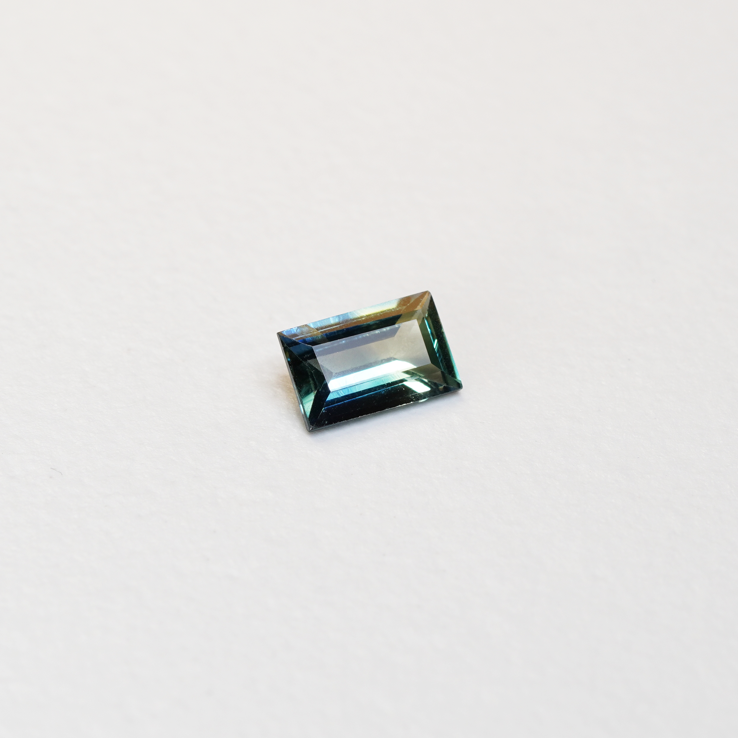 1.1 carat baguette parti teal sapphire with mixed green and blue color.