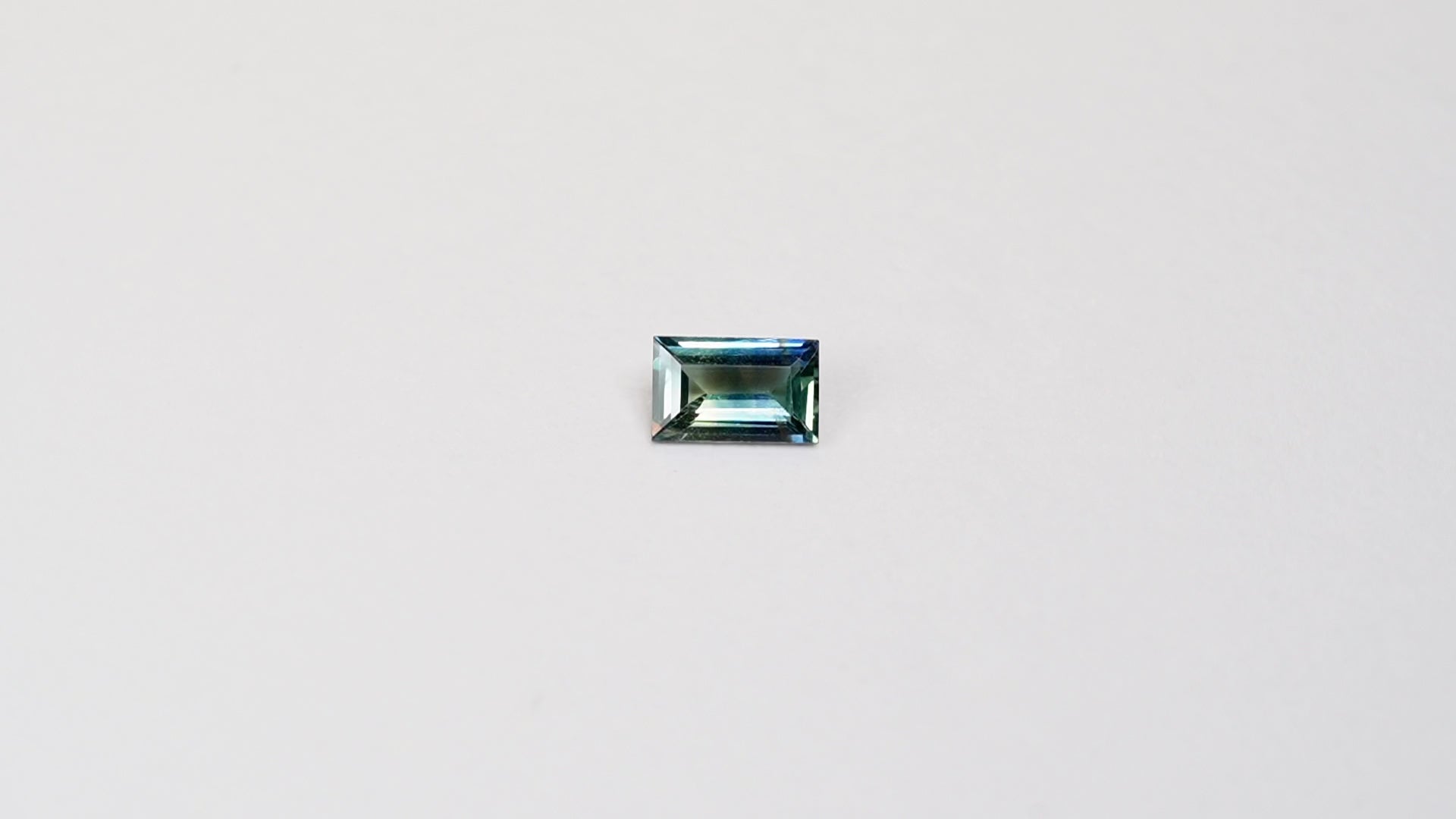 1.1 carat baguette parti teal sapphire with mixed green and blue color.